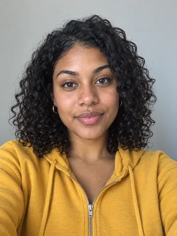Original selfie of a woman with dark curly hair in a mustard hoodie